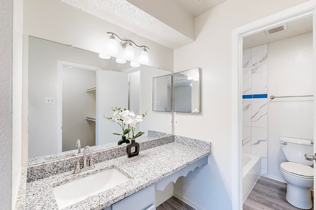 full bathroom with toilet, wood-type flooring, a textured ceiling, vanity, and shower / bath combination