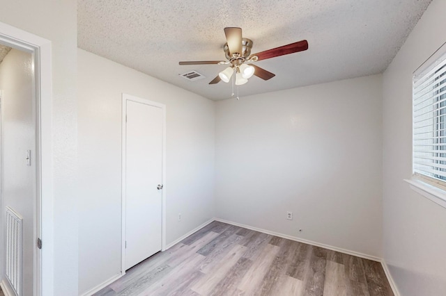 unfurnished bedroom with multiple windows, a textured ceiling, ceiling fan, and light wood-type flooring