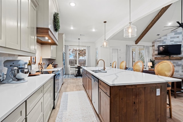 kitchen featuring appliances with stainless steel finishes, sink, light hardwood / wood-style flooring, pendant lighting, and a large island with sink