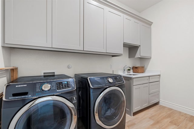 laundry room featuring sink, light hardwood / wood-style floors, cabinets, and independent washer and dryer