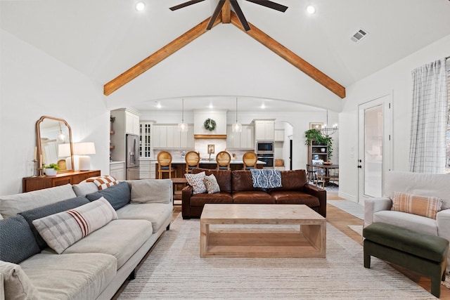 living room featuring light wood-type flooring, ceiling fan with notable chandelier, beamed ceiling, and high vaulted ceiling