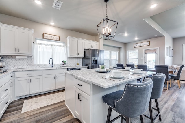 kitchen with a kitchen bar, stainless steel refrigerator with ice dispenser, white cabinets, a kitchen island, and sink