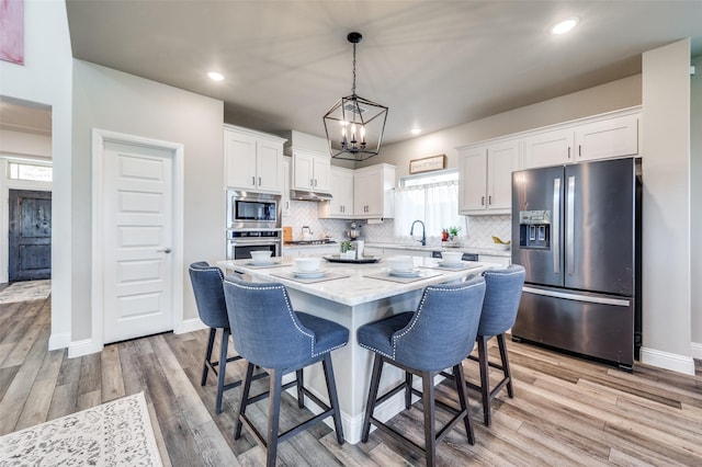 kitchen with a center island, decorative light fixtures, white cabinetry, stainless steel appliances, and tasteful backsplash