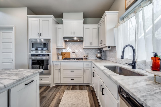 kitchen featuring white cabinets, appliances with stainless steel finishes, decorative backsplash, sink, and light stone counters