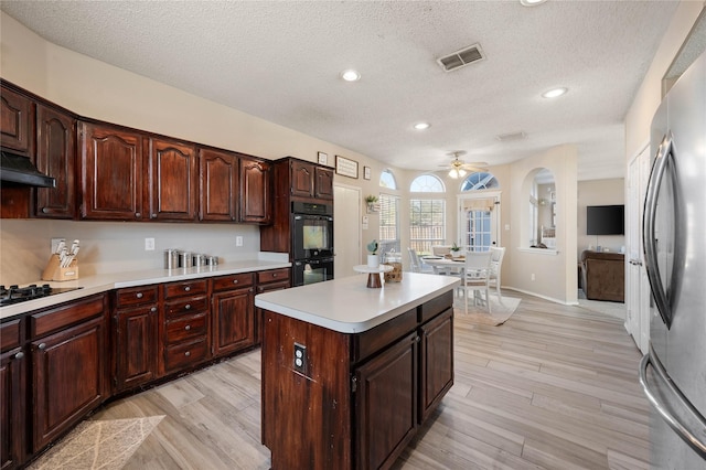 kitchen with black double oven, a center island, a textured ceiling, stainless steel refrigerator with ice dispenser, and sink