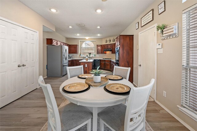 kitchen with double oven, stainless steel fridge with ice dispenser, a textured ceiling, a center island, and black dishwasher