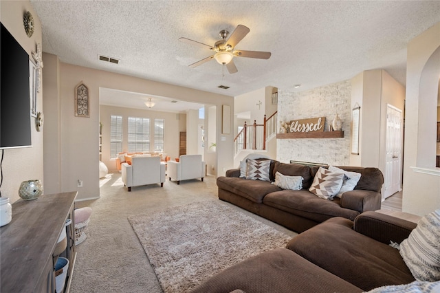 living room featuring ceiling fan, a textured ceiling, a fireplace, and carpet floors