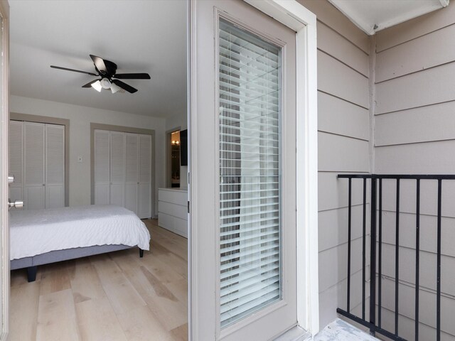 bedroom featuring multiple closets, light hardwood / wood-style floors, ceiling fan, wood walls, and multiple windows