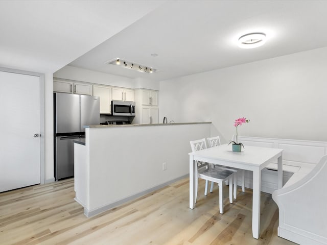 kitchen featuring kitchen peninsula, white cabinets, light wood-type flooring, and stainless steel appliances