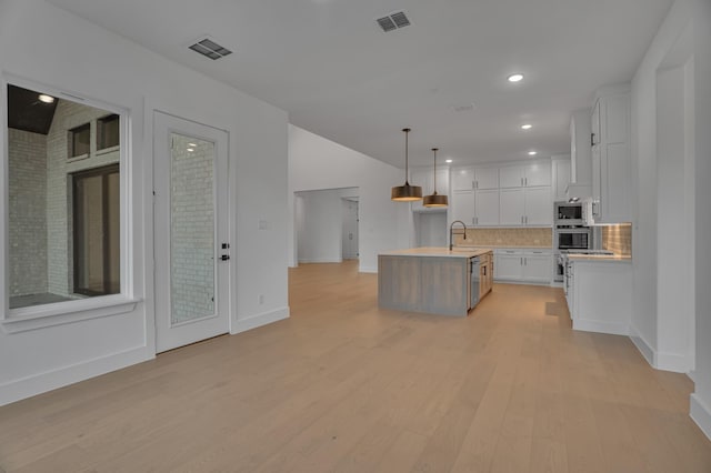 kitchen featuring white cabinetry, a kitchen island with sink, sink, pendant lighting, and backsplash