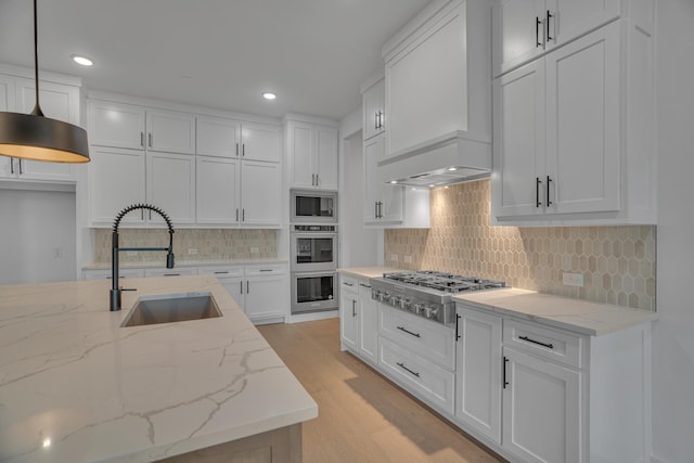 kitchen with pendant lighting, sink, white cabinets, light stone countertops, and stainless steel appliances