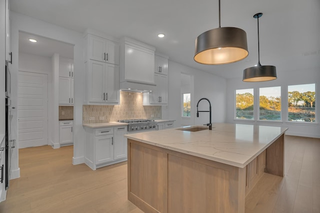 kitchen featuring white cabinets, sink, hanging light fixtures, light stone counters, and a center island with sink