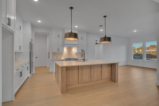 kitchen featuring white cabinets, decorative light fixtures, a kitchen island with sink, and sink