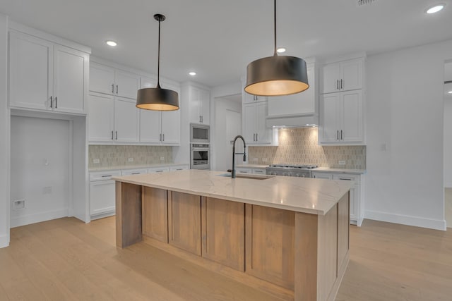 kitchen with decorative light fixtures, white cabinetry, stainless steel appliances, and an island with sink