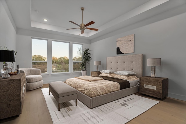 bedroom with ceiling fan, a raised ceiling, and light hardwood / wood-style flooring