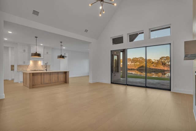 unfurnished living room with light hardwood / wood-style flooring, a towering ceiling, and an inviting chandelier