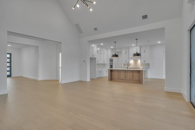 unfurnished living room featuring high vaulted ceiling, light hardwood / wood-style floors, and a notable chandelier