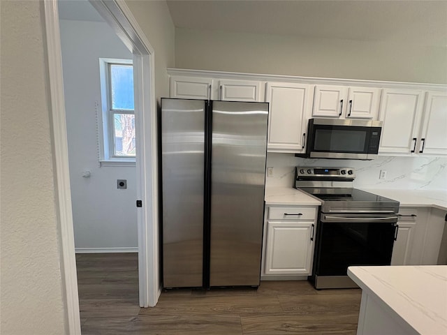 kitchen with light stone countertops, white cabinetry, stainless steel appliances, and dark wood-style flooring