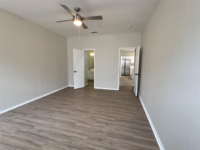 unfurnished bedroom with dark wood-style floors, visible vents, freestanding refrigerator, ceiling fan, and baseboards