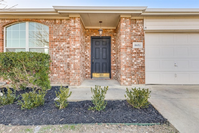 doorway to property with a garage, brick siding, and driveway