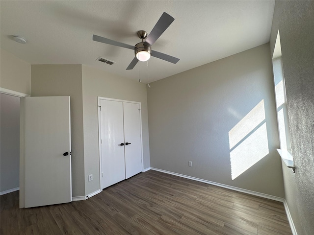 unfurnished bedroom with ceiling fan, wood finished floors, visible vents, baseboards, and a closet