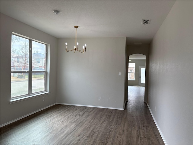 unfurnished room featuring arched walkways, dark wood-type flooring, visible vents, and baseboards