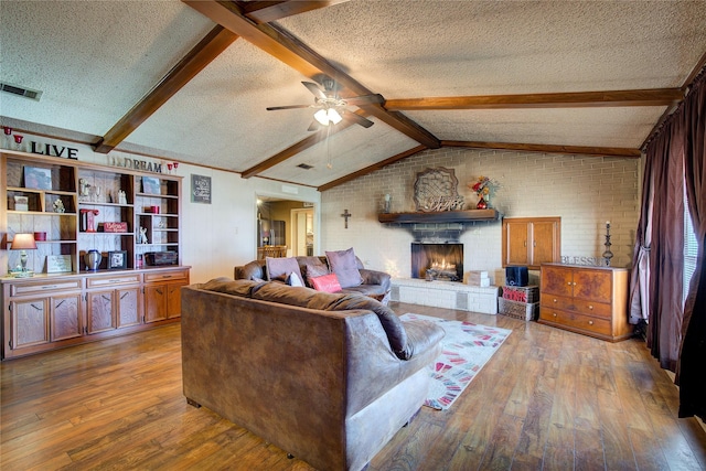 living room featuring a fireplace, a textured ceiling, light wood-type flooring, and vaulted ceiling with beams