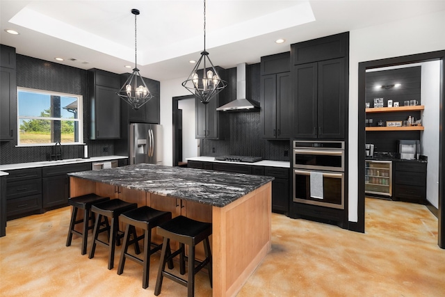 kitchen featuring a center island, wall chimney range hood, a raised ceiling, a breakfast bar, and stainless steel appliances