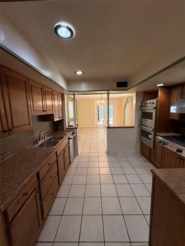 kitchen with stainless steel appliances, sink, backsplash, decorative columns, and light tile patterned floors