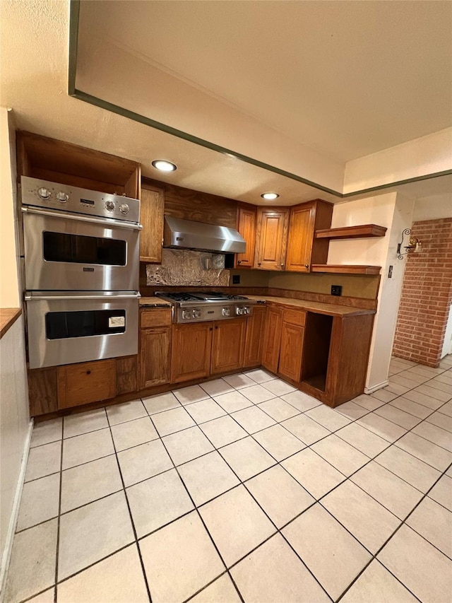 kitchen with brick wall, wall chimney exhaust hood, stainless steel appliances, tasteful backsplash, and light tile patterned flooring