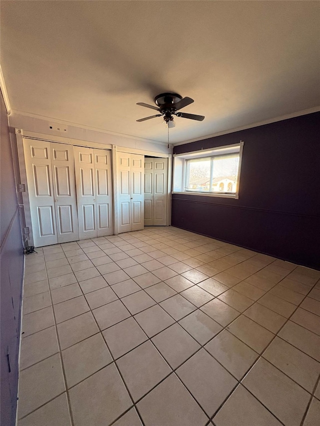 unfurnished bedroom with two closets, light tile patterned floors, ceiling fan, and ornamental molding