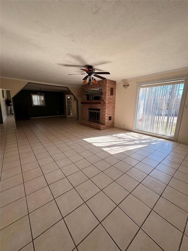 unfurnished living room with a brick fireplace, a textured ceiling, light tile patterned floors, and ceiling fan