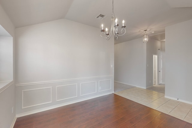 empty room with wood-type flooring, an inviting chandelier, and lofted ceiling