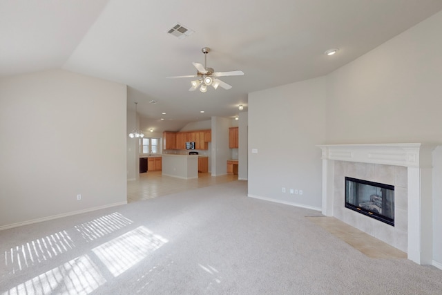 unfurnished living room featuring ceiling fan, light carpet, a tiled fireplace, and vaulted ceiling