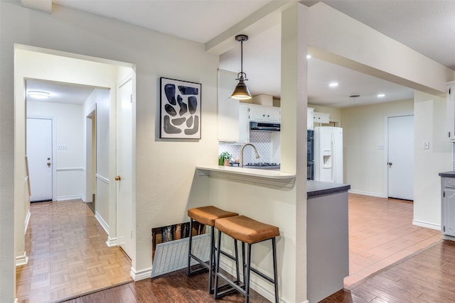 kitchen with kitchen peninsula, a breakfast bar area, white fridge with ice dispenser, and white cabinets