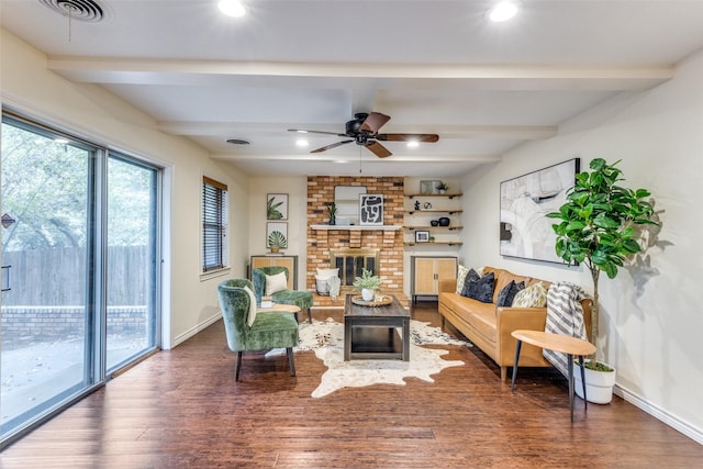 living room featuring dark wood-type flooring, ceiling fan, beam ceiling, and a brick fireplace