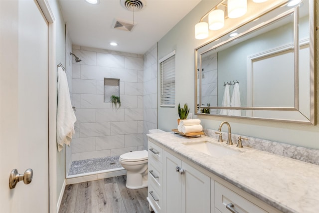 bathroom featuring vanity, tiled shower, hardwood / wood-style floors, and toilet