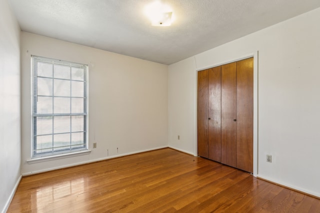 unfurnished bedroom featuring wood-type flooring, multiple windows, a textured ceiling, and a closet