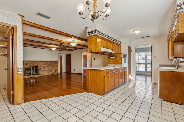 kitchen with white appliances, hanging light fixtures, a tile fireplace, light tile patterned floors, and kitchen peninsula