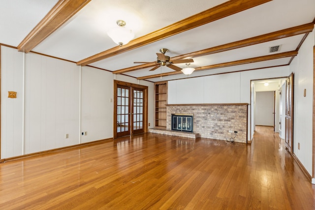 unfurnished living room with french doors, built in features, a brick fireplace, light hardwood / wood-style flooring, and beam ceiling