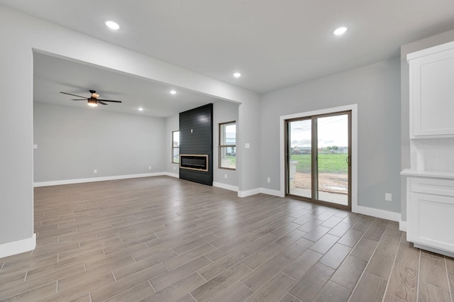 unfurnished living room with a fireplace, light wood finished floors, ceiling fan, and baseboards