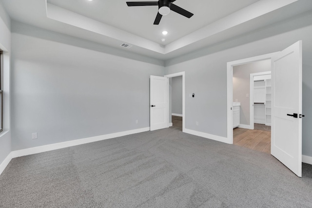 unfurnished bedroom with carpet, visible vents, a tray ceiling, and baseboards