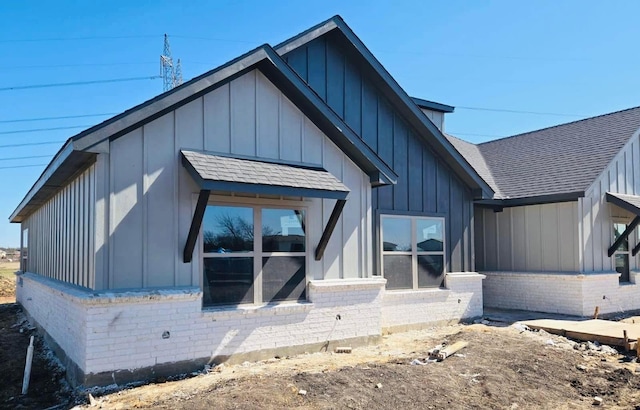 back of property with a shingled roof, board and batten siding, and brick siding