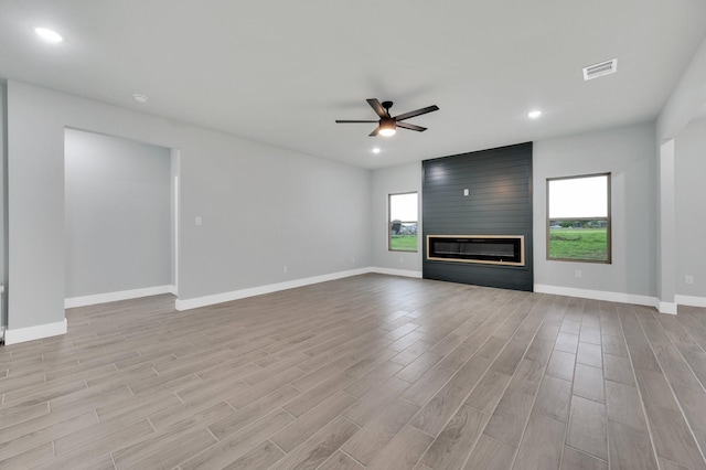 unfurnished living room with wood finished floors, a fireplace, baseboards, visible vents, and a ceiling fan