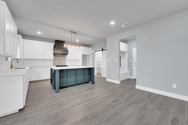 kitchen with a sink, a barn door, visible vents, baseboards, and premium range hood