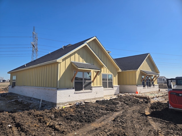 view of side of property with board and batten siding, brick siding, and roof with shingles