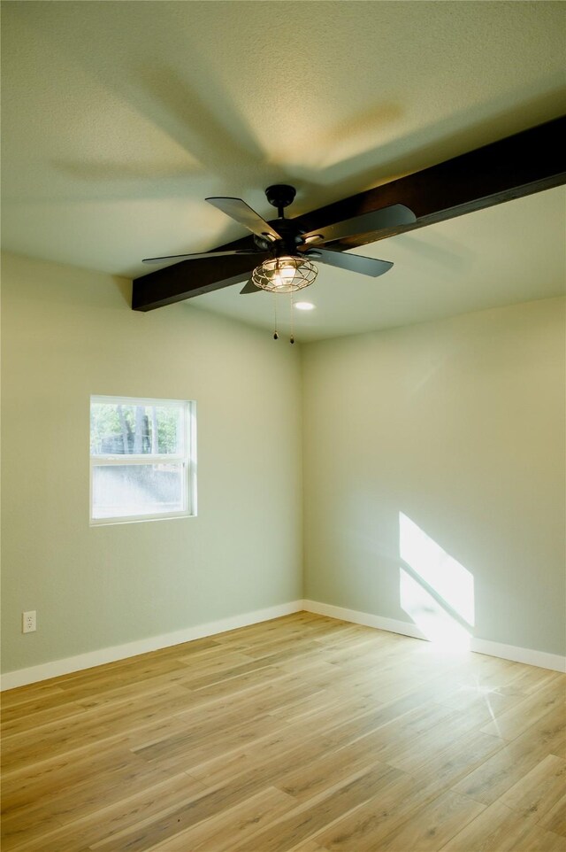 empty room with ceiling fan, light hardwood / wood-style flooring, and beamed ceiling