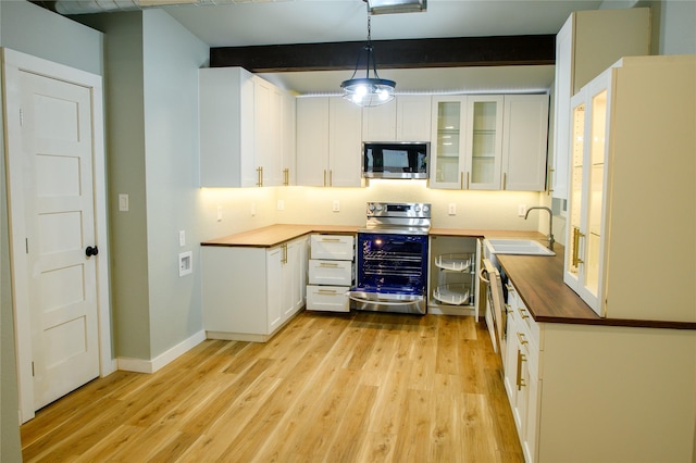 kitchen featuring appliances with stainless steel finishes, sink, white cabinets, hanging light fixtures, and light wood-type flooring