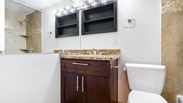 bathroom with a tile shower, toilet, and vanity