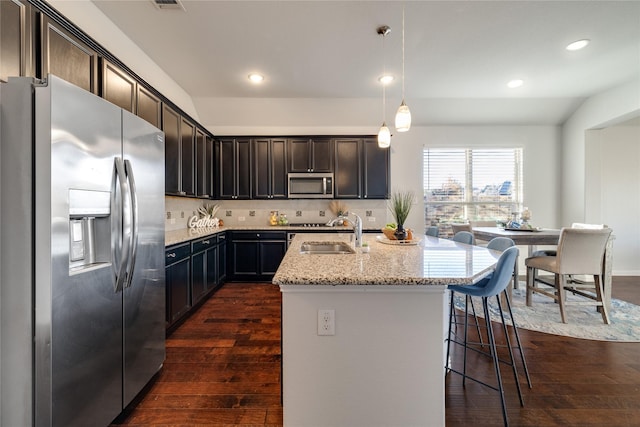 kitchen featuring sink, decorative light fixtures, stainless steel appliances, light stone countertops, and a kitchen island with sink